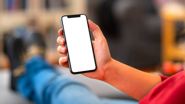 femme retenant le téléphone intelligent blanc blanc d’écran à la maison - regarder par dessus son épaule photos et images de collection