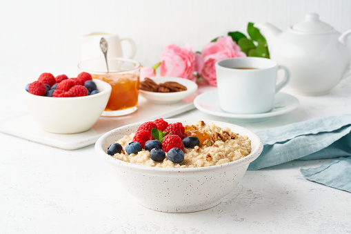 Oatmeal porridge with blueberry, raspberries, jam and nuts in white bowl, dash diet with berries, white background, side view. Healthy diet breakfast