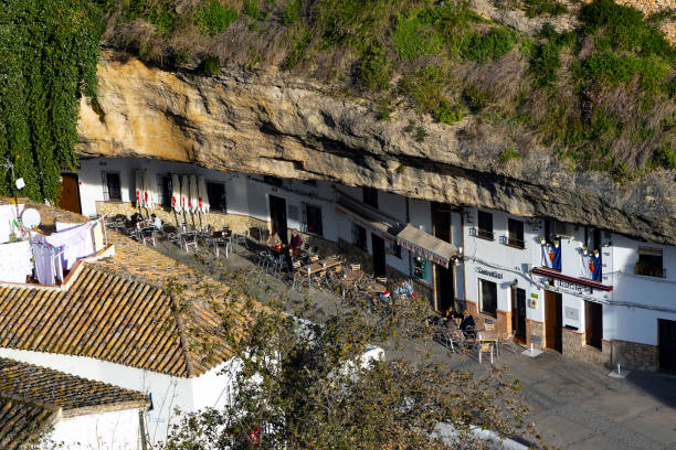 Named after its once flourishing wineries - bodegas - Setenil is probably unique among the pueblos blancos, white villages, of Andalucia. Where most pueblos blancos were built on protective bluffs and pinnacles, this town grew out of a network of caves in the cliffs above the rio Trejo north-west of Ronda. Its blinding white houses seem to emerge from the rocks, and some have rock roofs and even olive groves on their roofs.