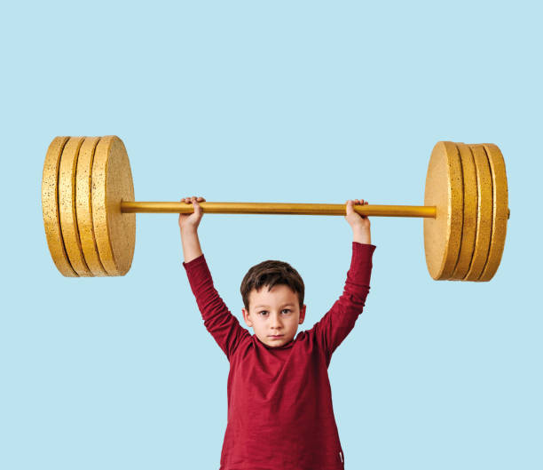 istock Cute child lifting gold barbell on blue pastel background. He is a determined and successful child. 1208352453