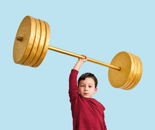 istock Cute child lifting gold barbell on blue pastel background. He is a determined and successful child. 1208352631