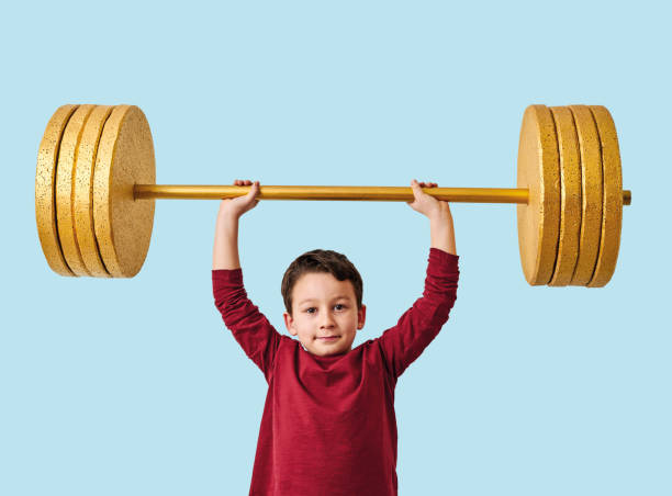 istock Cute child lifting gold barbell on blue pastel background. He is a determined and successful child. 1208352720
