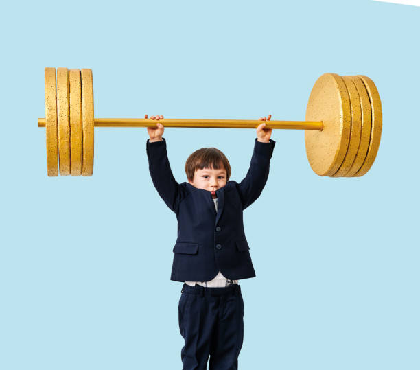 istock Cute child lifting gold barbell on blue pastel background. He is a determined and successful child. 1208352823