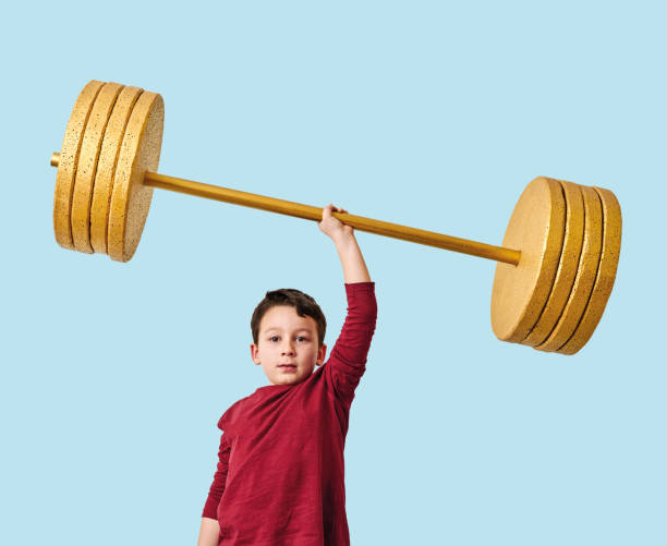 istock Cute child lifting gold barbell on blue pastel background. He is a determined and successful child. 1208353041