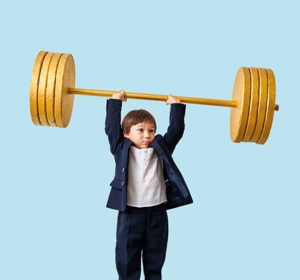 istock Cute child lifting gold barbell on blue pastel background. He is a determined and successful child. 1208353060