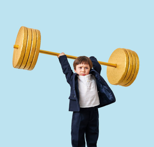 istock Cute child lifting gold barbell on blue pastel background. He is a determined and successful child. 1208353820