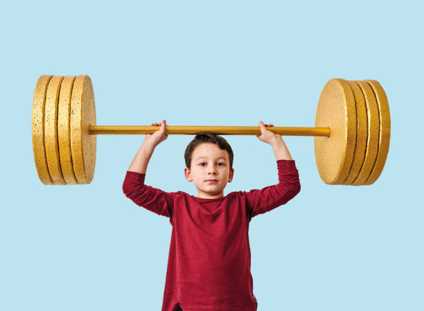 istock Cute child lifting gold barbell on blue pastel background. He is a determined and successful child. 1208354080