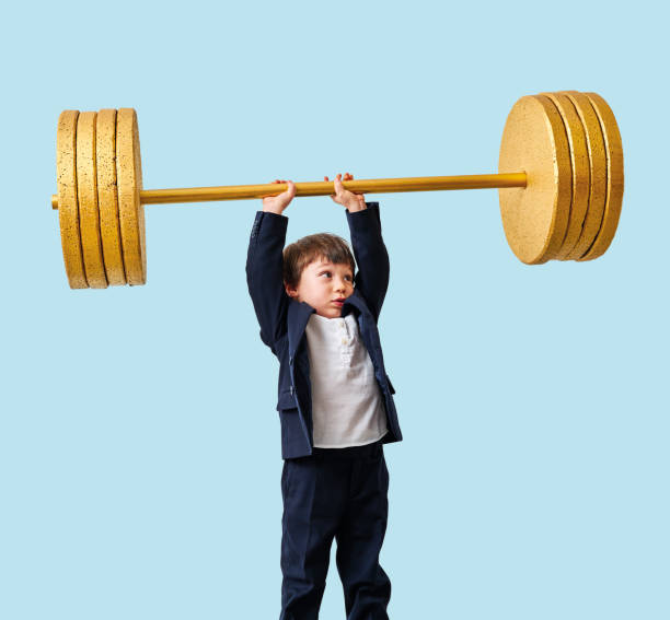 istock Cute child lifting gold barbell on blue pastel background. He is a determined and successful child. 1208354423