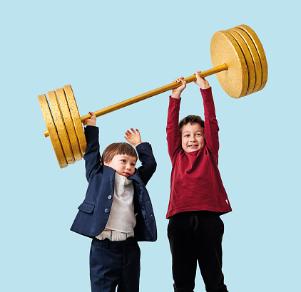 Two children lifting gold barbell on blue pastel background. They are determined and successful children.