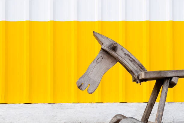 An old  wooden pony in front of a white and yellow galvanized steel wall.