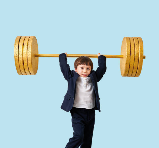 istock Cute child lifting gold barbell on blue pastel background. He is a determined and successful child. 1208354768