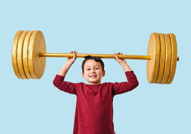 istock Cute child lifting gold barbell on blue pastel background. He is a determined and successful child. 1208354914