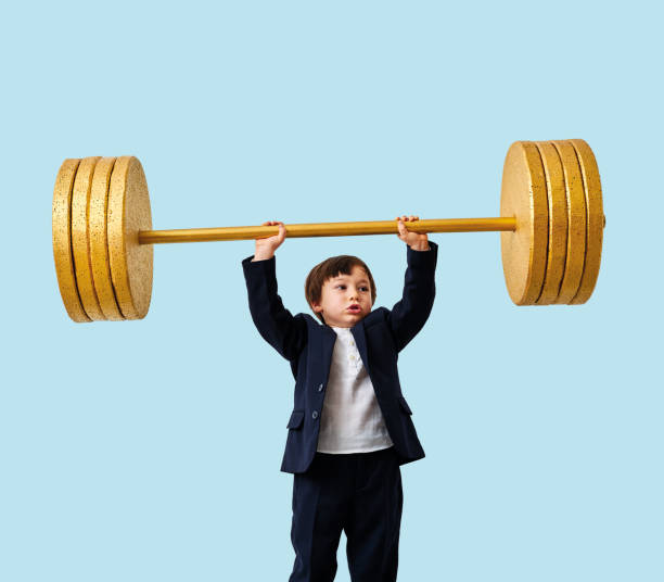 istock Cute child lifting gold barbell on blue pastel background. He is a determined and successful child. 1208354927