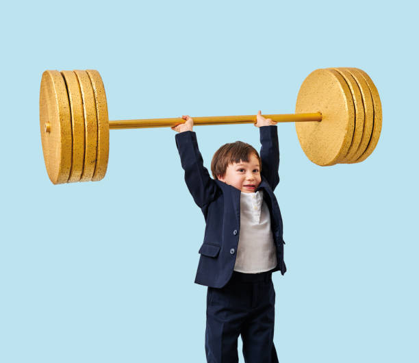 istock Cute child lifting gold barbell on blue pastel background. He is a determined and successful child. 1208355158