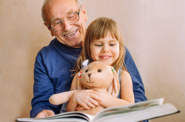 красивая маленькая девочка читает книгу со своим дедом - grandparent grandfather granddaughter little girls стоковые фото и изображения