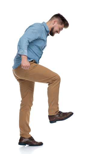 Side view of a young casual man stepping and laughing on white studio background