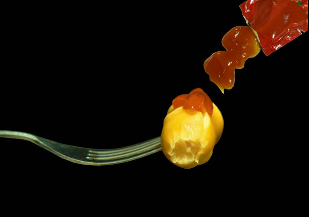 fried pork sausage slice stabbing in silver fork and dressing ketchup from sachet isolated on black background