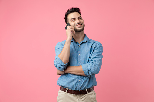 happy young guy smiling and talking on the phone, looking to side on pink background