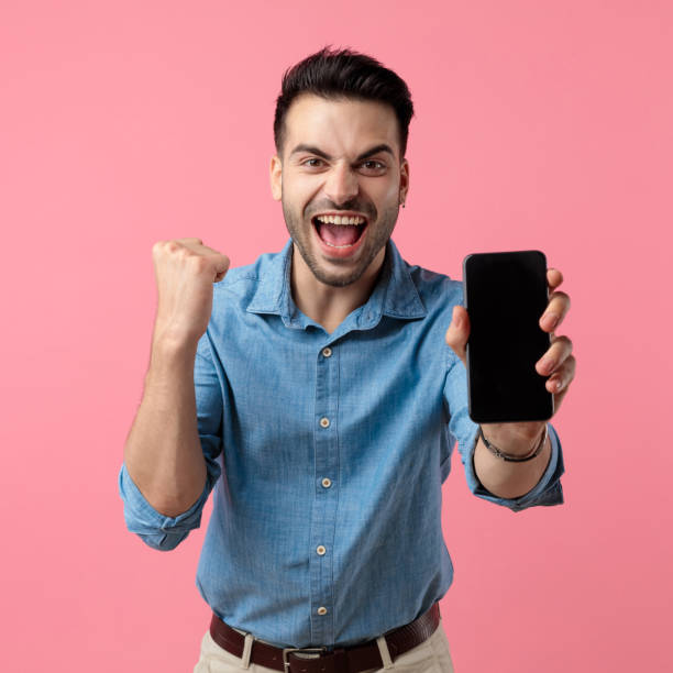 istock young casual guy showing black empty screen and celebrating victory 1208374486