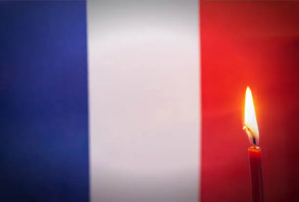 Burning candle on the background of the flag of France. The concept of mourning and sorrow in the country
