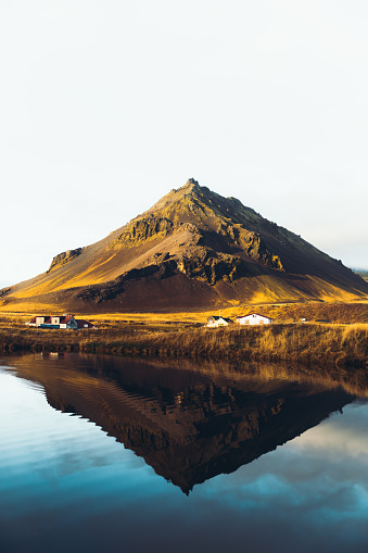 Scenic view if the beautiful triangle-shaped mountain, reflection lake and a small village during bright sunny day on the West Iceland