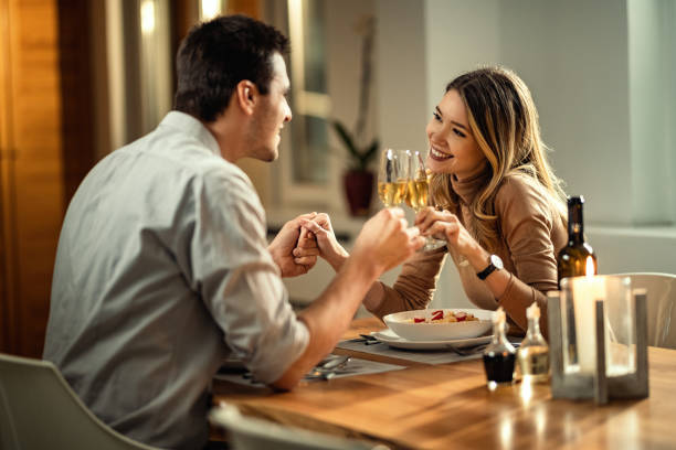 gelukkig paar dat met champagne tijdens diner bij eettafel roostert. - romantic stockfoto's en -beelden