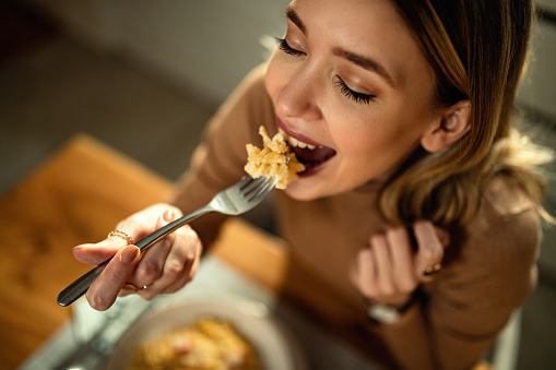 Primer plano de joven mujer feliz comiendo pasta en la mesa de comedor. photo