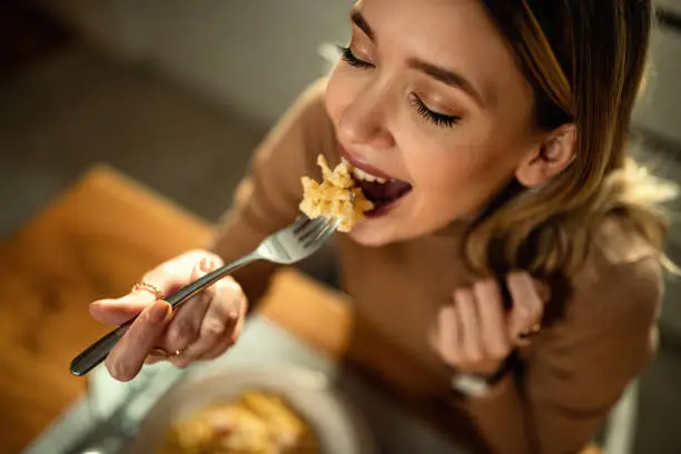 Photo of Close-up of young happy woman eating pasta at dining table.