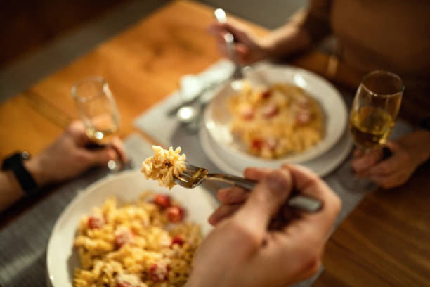 istock Close-up of couple eating pasta for dinner at dining table. 1208380065