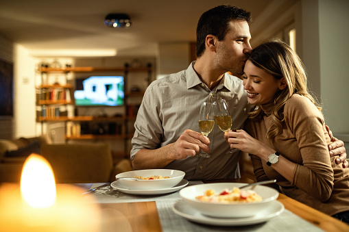 Affectionate man kissing his girlfriend while toasting with Champagne during dinner at dining table.