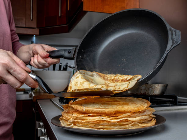 istock Human hands holding a spatula and a frying pan spread hot pancake on the dish from which steam comes. Home kitchen. 1208381830