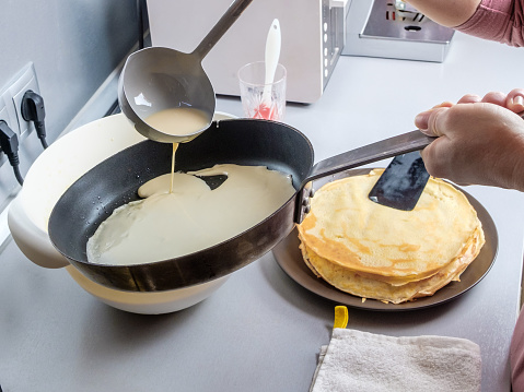 Batter pouring out of a metal bucket onto a red-hot greased frying pan. The process of baking pancakes. Traditional treat for the holiday of Maslenitsa.