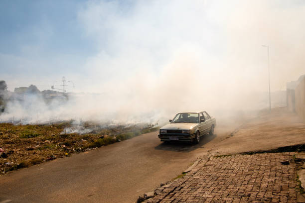Johannesburg, South Africa - March 31, 2017: A car drives by a burning and smoking field lit on fire for construction along the streets of Johannesburg’s Soweto township, the largest township in South Africa.