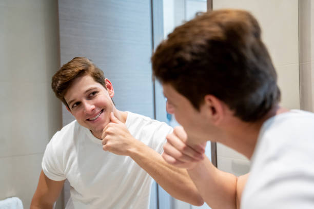 istock Happy young man admiring his face while looking at mirror smiling 1208382259