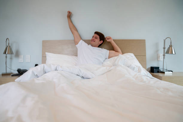 istock Handsome man waking up and stretching his arms while sitting on bed 1208382276