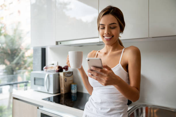 istock Cheerful young woman leaning against kitchen counter texting on smartphone while enjoying a coffee 1208382318
