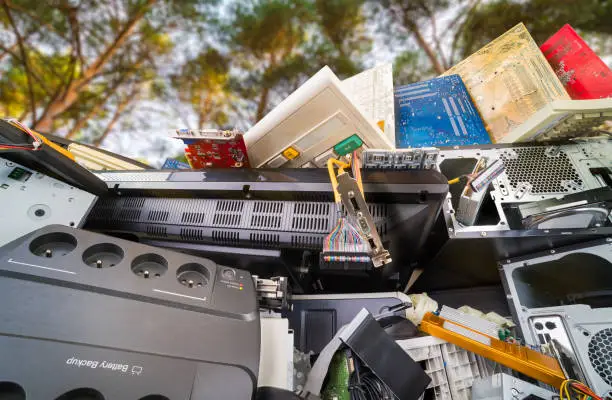 Photo of Electronic waste detail. Discarded computer hardware components on pile under trees with sunny sky