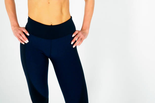 View of the athletic muscular belly and hips of a young woman in athletic tight-fitting trousers on a white background. View of the athletic muscular belly and hips of a young woman in dark athletic tight-fitting trousers on a white background. Sexy girl holds her hands on her hips, demonstrating developed muscles. красота stock pictures, royalty-free photos & images