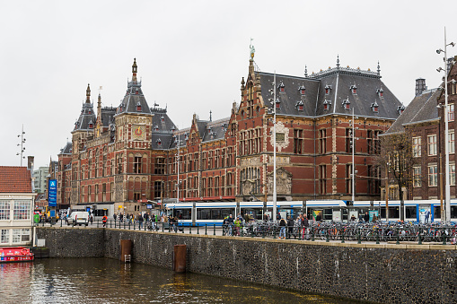 Amsterdam, Netherlands - November 28, 2019: View of the Central Railway Station facade and transport, channel.