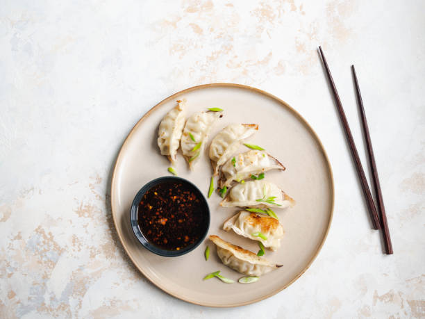 Chinese traditional dumplings - gyoza with pork and vegetables on a round plate with soy sauce in a bowl. Top view. Chinese traditional dumplings - gyoza with pork and vegetables on a round plate with soy sauce in a bowl. chinese dumpling stock pictures, royalty-free photos & images
