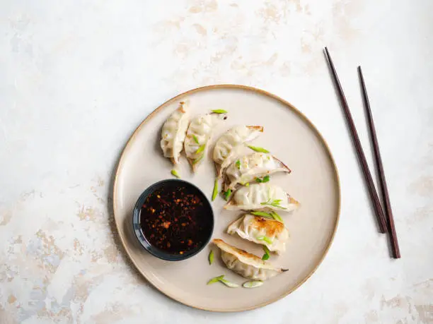 Photo of Chinese traditional dumplings - gyoza with pork and vegetables on a round plate with soy sauce in a bowl. Top view.