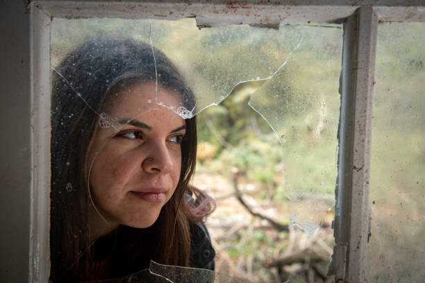 istock Young woman posing behind a broken window 1208388759