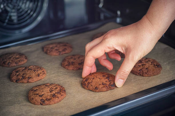 Person taking baked homemade chocolate chip cookie from baking tray. Close up.