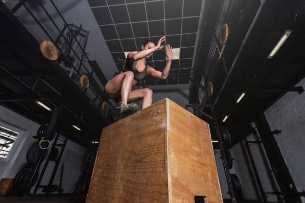 giovane ragazza muscolosa dalla vestibilità sudata forte con grandi muscoli che fanno box jump allenamento cross workout hardcore in palestra movimento di messa a fuoco selettiva confondere le persone reali - sporting position vitality blurred motion strength foto e immagini stock