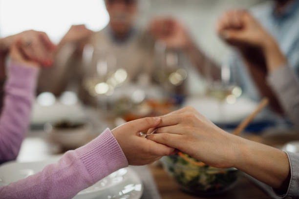 primo piano di genitore e figlio che si tengono per mano mentre dicono grazia prima di un pasto. - saying grace immagine foto e immagini stock