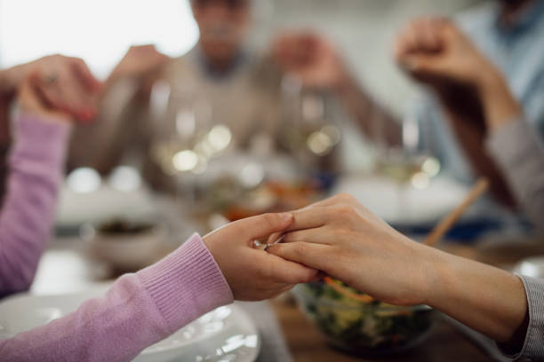 Close-up of parent and child holding hands while saying grace before a meal. Close-up of extended family holding hands and saying grace before the lunch at dining table. saying grace stock pictures, royalty-free photos & images