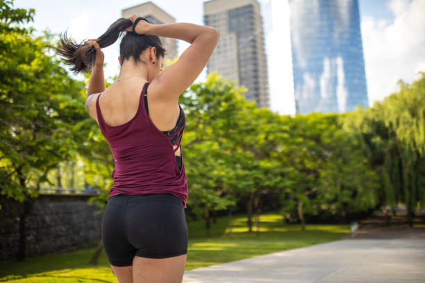 Young Latin woman tying her hair before exercising outdoors Rear view of female athlete tying her hair in ponytail and getting ready for running in public park, rear view woman tying hair in ponytail getting ready for exercising stock pictures, royalty-free photos & images