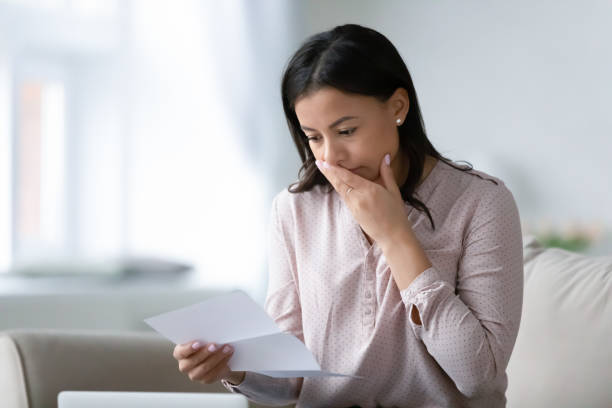 Unhappy biracial woman read bad news in letter Distressed African American young woman sit on couch at home read bad negative news in paper correspondence, unhappy biracial female stressed consider unpleasant message in postal letter eviction photos stock pictures, royalty-free photos & images