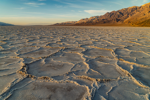 Salt flats in Badwater Basin in Death Valley national park , California during sunset with majestic mountains.