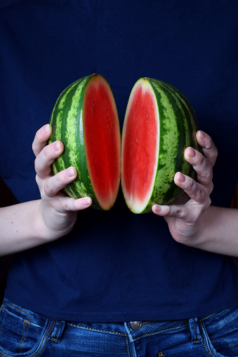Mini watermelon cut into two halves held in woman hands